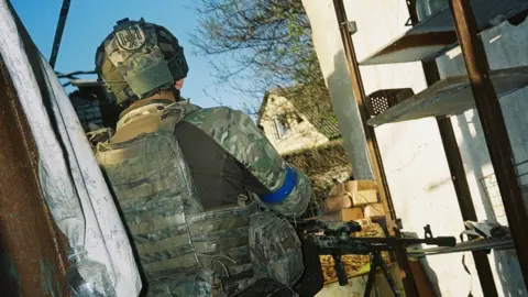 Conall Kearney A unformed Ukrainian soldier stands outside, holding a gun