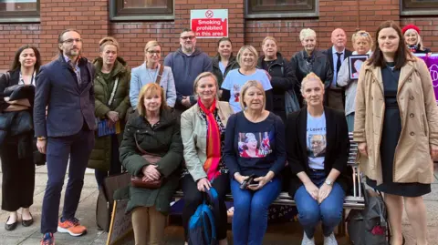 Steve Jones/BBC Group of people stood and sitting outside red brick building