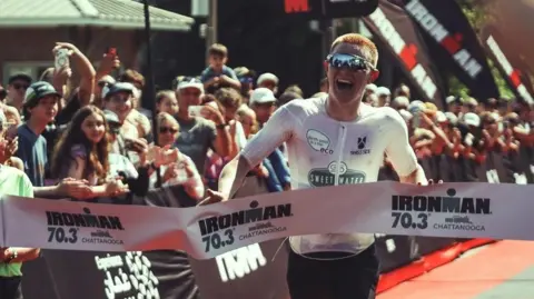 Shot by Pierson A photo of man wearing sunglasses crossing the finish line of a competition 