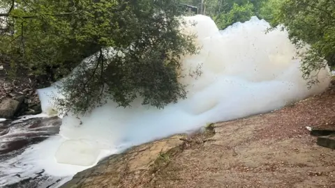 Craig Hannah Large white clumps of foam in a river.