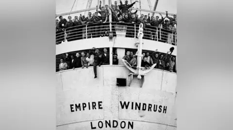 PA Media A black and white image of HMT Empire Windrush when it arrived in Tilbury in 1948. Passengers wave and smile from the ship.