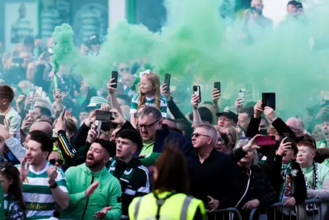 PA Media Celtic fans ahead of the William Hill Premiership match at Celtic Park, Glasgow. Several fans are filming on their phones while one lets off green smoke. 