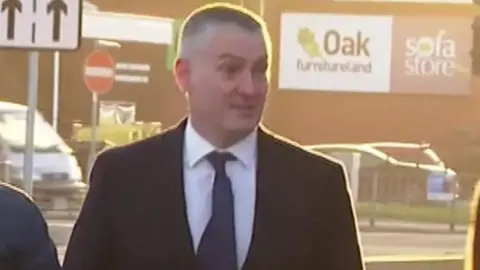 Richard Williams in dark suit and navy tie. 