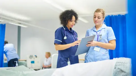 Getty Images A stock image showing two nurses at a patient's bedside in a hospital