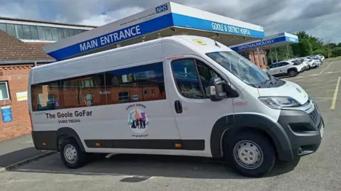 A white minibus with the "Goole GoFar" logo, parked in a car park outside Goole & District Hospital