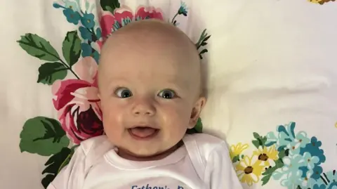 A happy-looking baby lies on a flowery cushion. 