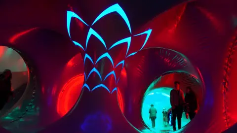 The inside of a giant inflatable sculpture which is lit up red and blue. People can be seen walking through it. 