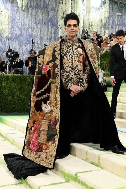 Getty Images Karan Johar wears a vintage jacket under a hand-painted cape with detailed embroidery. Johar's team described the paintings featured on his outfit as characters from Indian mythology.