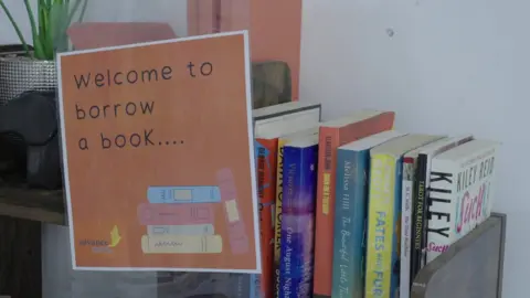 A selection of books on a shelf, with a poster that states: Welcome to borrow a book...
