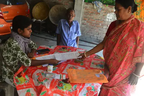 NurPhoto via Getty Images Booth Level Officers (BLO) and their workers check and collect the filling of enumeration forms. Voters fill up and queue to submit the forms for the special intensive revision (SIR) of electoral rolls in Ghogomali village area in Siliguri, India, on November 22, 2025. (Photo by Diptendu Dutta/NurPhoto via Getty Images)