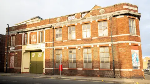 Sunderland City Council The two-storey red-bricked building has large green doors with the letters "P" and "S" painted on them. There are several large boarded-up windows.
