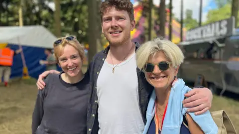 Jon Wright/BBC Actors Charlie Cameron and Joe McArdle with INK director Julia Sowerbutts stand together in front of festival tents