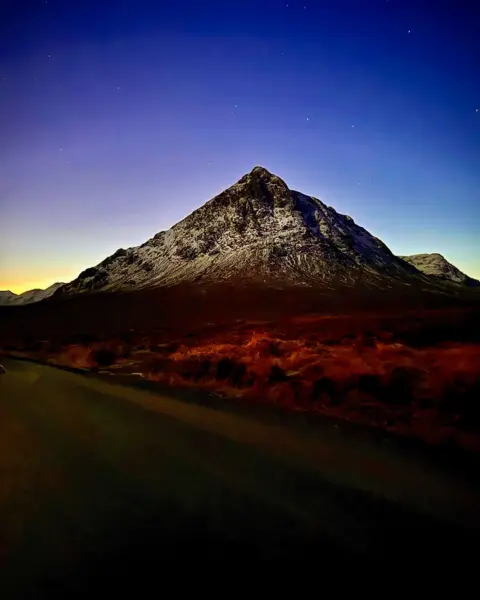 Mark Reynolds Portrait image of Buachaille Etive Mòr below a dark blue sky with sun peeking above the horizon slightly