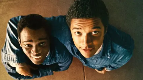 Amazon MGM Studios Brandon Wilson and Ethan Herisse in Nickel Boys, both wearing denim jackets and looking at their reflections in a ceiling mirror