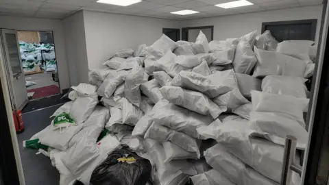 Two large piles of bags, most of them white, are in two adjoining rooms.