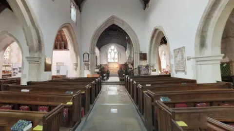 Google  A google maps image of the interior of St Michael's Church Betchworth showing the aisle, rows of pews, pillars and traditional stained glass windows