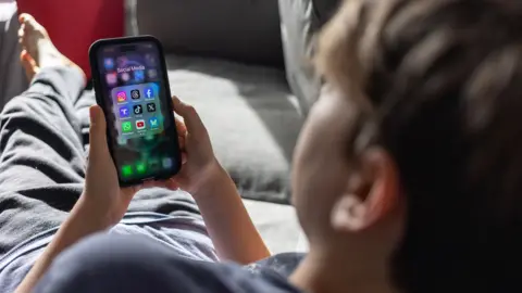 A child lies on a couch holding a smartphone looking at social media apps