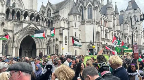PA Media General view of people stood outside the Royal Courts of Justice building in London. A number of Palestinian flags can be seen