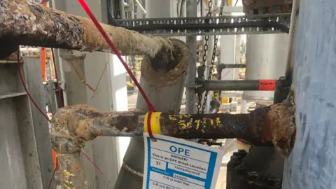 HSE Corroded piping at the Mossmorran plant, with a label around one pipe saying "DANGER This is an OPE Break Location"
