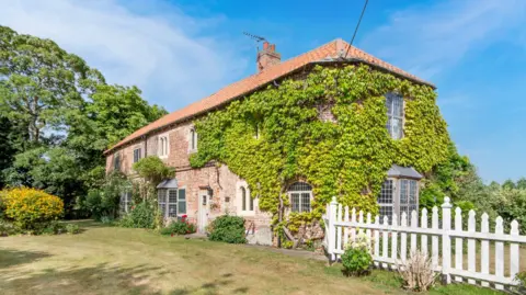 An manor house surrounded by trees with a white fence