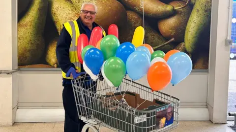 Julie Bushby Tony Johnson is smiling at the camera and standing with a shopping trolley full of colourful balloons