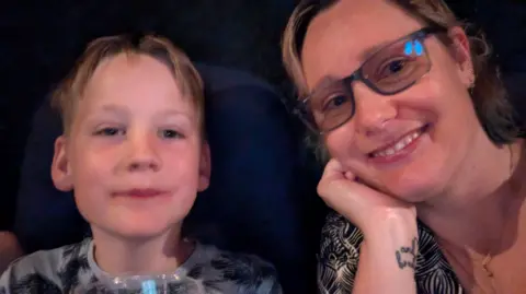 Family handout Monty and his mum Emily smiling as they take a selfie in front of a colourful wall.
