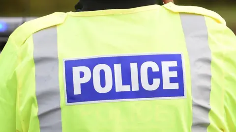 A police officer wearing a fluorescent jacket with POLICE in large white letters on a blue background