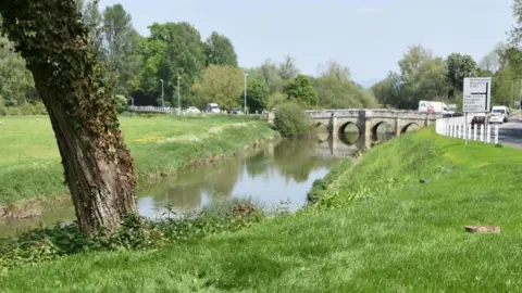 Dorset Council River Stour flowing under the Sturminster Newton Bridge with cars travelling across the bridge and on the roads connected to it.