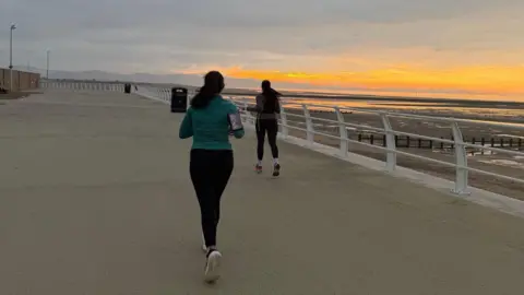 North Wales Police Two women running on Rhyl's coastline in North Wales with a sunset in the background 