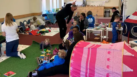 BBC A group of young children playing at a nursery class, with families and staff