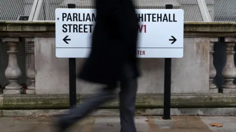 An unknown pedestrian passes a sign on Whitehall in London