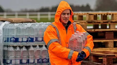 Getty Images A man in a hooded hi-vis orange jacket and black gloves is holding a pack of bottled water
