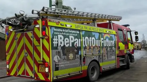 A red and yellow fire engine branded with the words "Suffolk Fire and Rescue Service". A recruiting advertisement is on the side of the engine and contains the slogan, "#BePartOfOurFuture". 