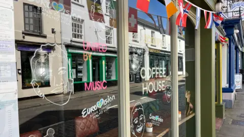 Scoff's Coffee Shop in Coleford, with drawings of Olly Alexander and Eurovision stickerson the window, along with bunting hung up 