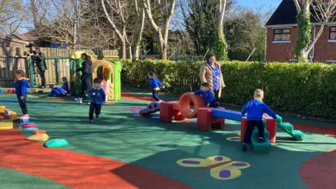 Children in a nursery uniform playing in a playground.