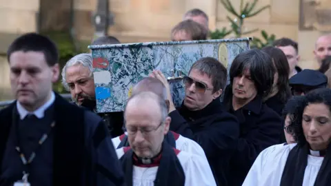 PA Mani's former Stone Roses and Primal Scream bandmates, along with Oasis star Liam Gallagher, carrying his coffin out of the cathedral. The coffin was painted like the cover of the Stone Roses first album.