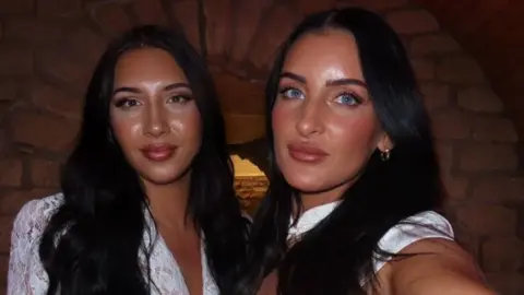 Lucy Robertson Two woman, both with dark hair and wearing white tops are looking at the camera