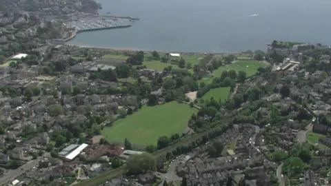 An aerial view of Torbay, there are houses dotted around in sections with sections of green grass. There is also the sea.