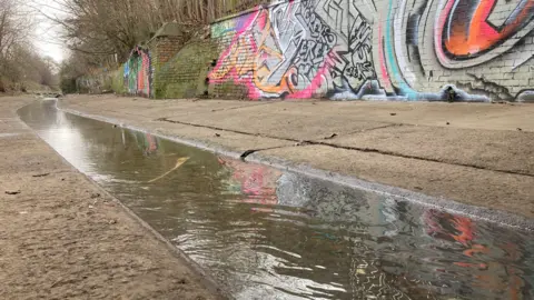 You can see the channel of water (a culvert) running through the middle of the picture. There is hard concrete on each side and this shows where the litter and other rubbish has been cleared away.