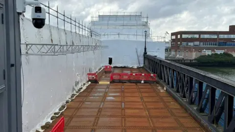 North East Lincolnshire Council Grimsby's Corporation Road Bridge is partially covered by white protective sheeting as restoration work continues. Brown decking can be seen, along with dark-grey railings.