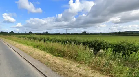 Google Maps A field with clouds above and foliage and hedges by a road verge