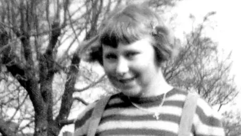 Jean Flannery née Blane A black and white photo of Jean Flannery née Blane. She is wearing a stripy top and is smiling at the camera.