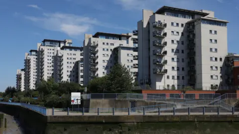 Royal Artillery Quays sits on the banks of the River Thames in Thamesmead, the buildings are high-rise, with a grey/white exterior. 
