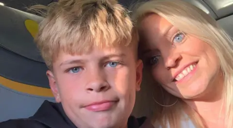 Family Handout Mikey Roynon (L) sitting next to his mother Hayley Ryall. They both have blonde hair and blue eyes and are smiling.