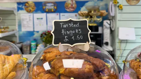 An assortment of pastries. A label says "twisted fingers, £1.50"