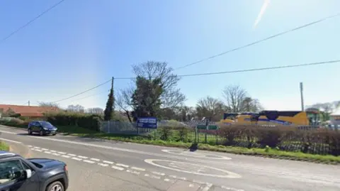 A Google image of a road junction shows part of a car driving towards a larger road, with another car on the left. There is an industrial unit in the background.