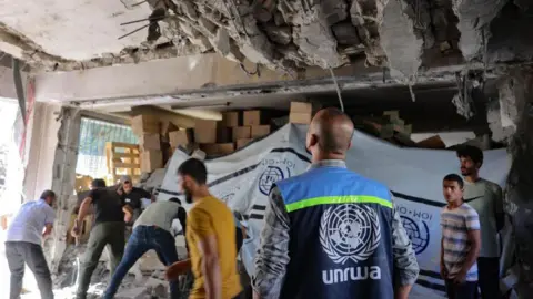 AFP An UNRWA worker and displaced Palestinians check the damage inside a UN school-turned-refuge in Gaza City (pictured: October 19, 2024.)