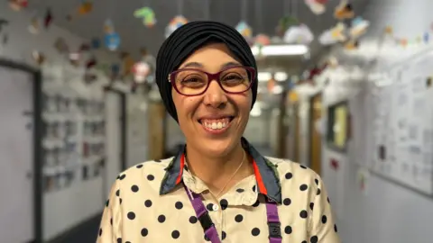 A doctor wearing a scarf, glasses and a spotted T-shirt.