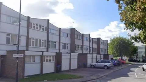a Google Streetview image of Tillett Close, showing a row of white and brick buildings and parked cars