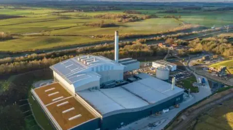 An industrial site, photographed from the sky against the backdrop of sprawling green fields and a motorway.
